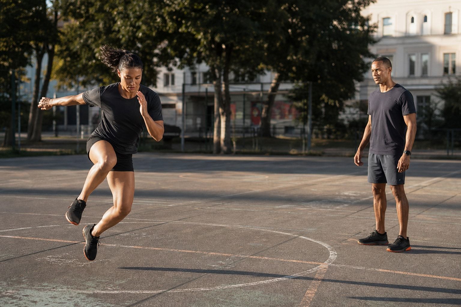 Sportlerin in einem seitlichen Einbein-Sprung über eine Linie auf einem Berliner Freiplatz, Julio Abad Veria beobachtet die Bewegung aus der Distanz.