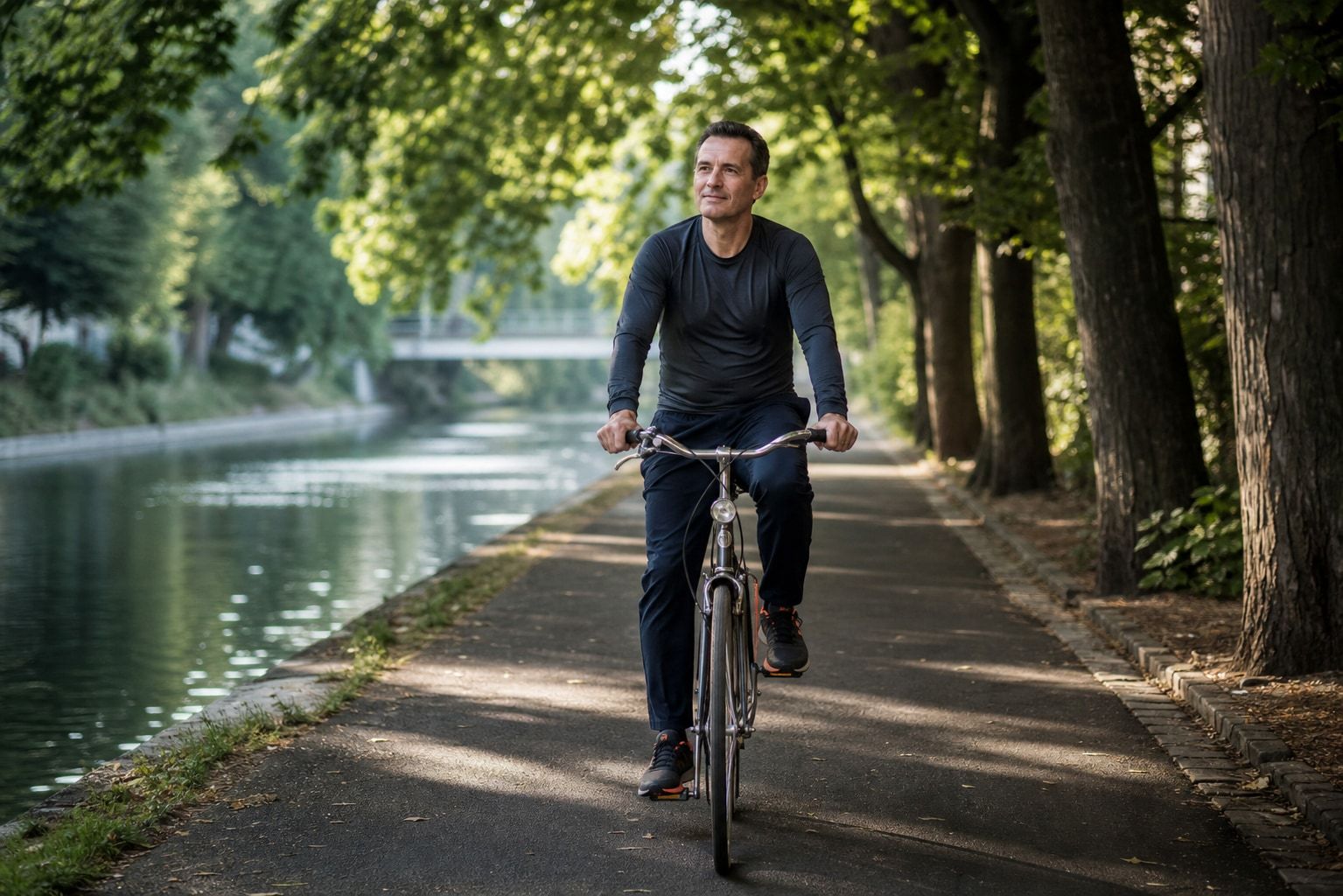 Trainierender fährt in ruhiger Trittfrequenz auf einem Rad über einen von Bäumen gesäumten Uferweg am Landwehrkanal.